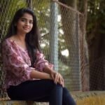 A smiling young woman poses outdoors in Thane, India, next to a chain-link fence.